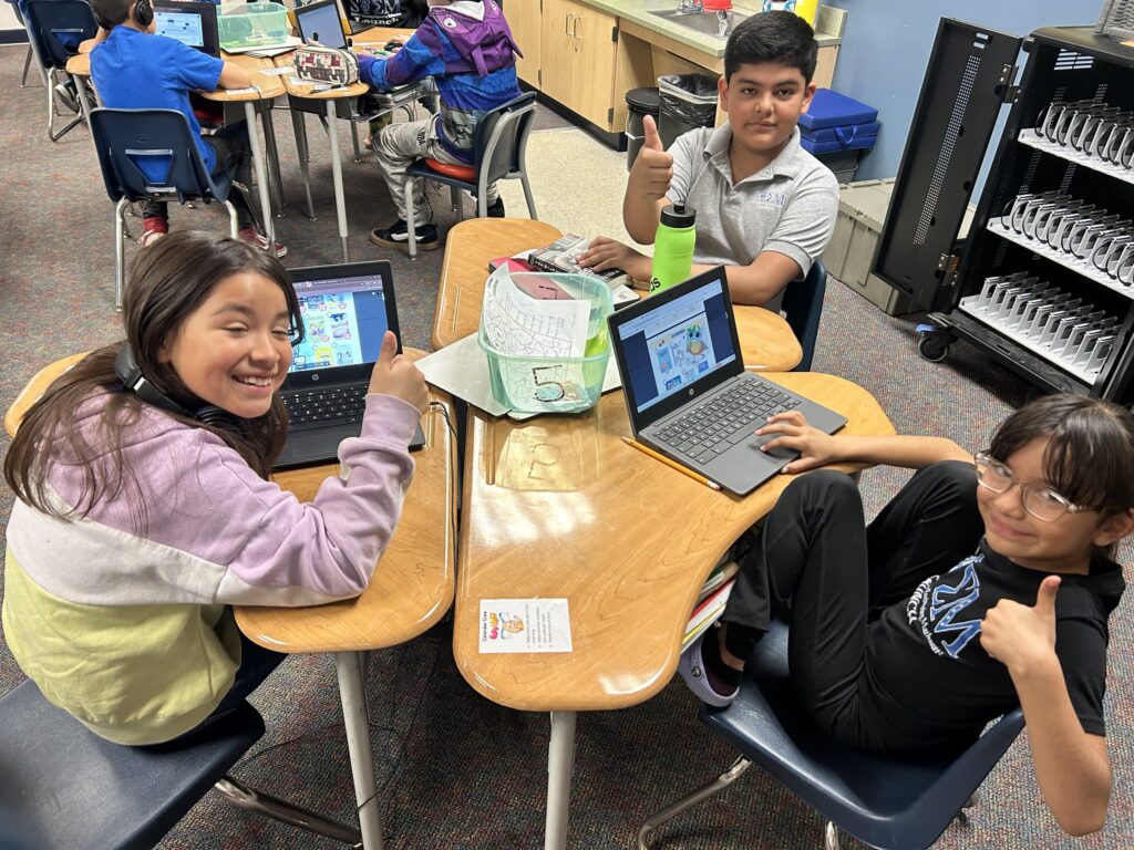 Students smile as they look at book options on laptops at their desks.