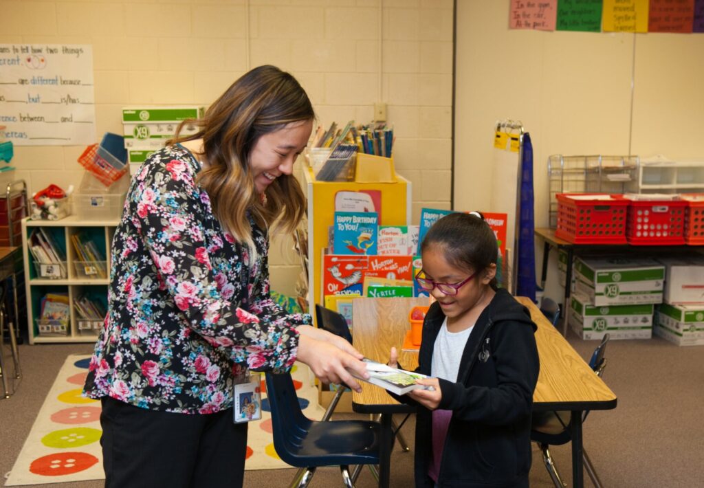 A teacher in a classroom hands a student their new Book Trust book.